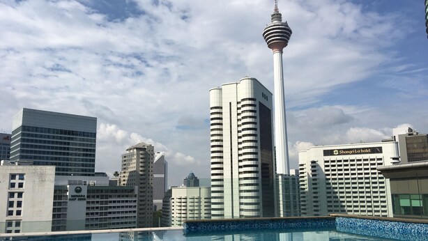 Un hôtel moderne doté d’une piscine, entouré d’immeubles de grande hauteur, avec une tour imposante en arrière-plan.