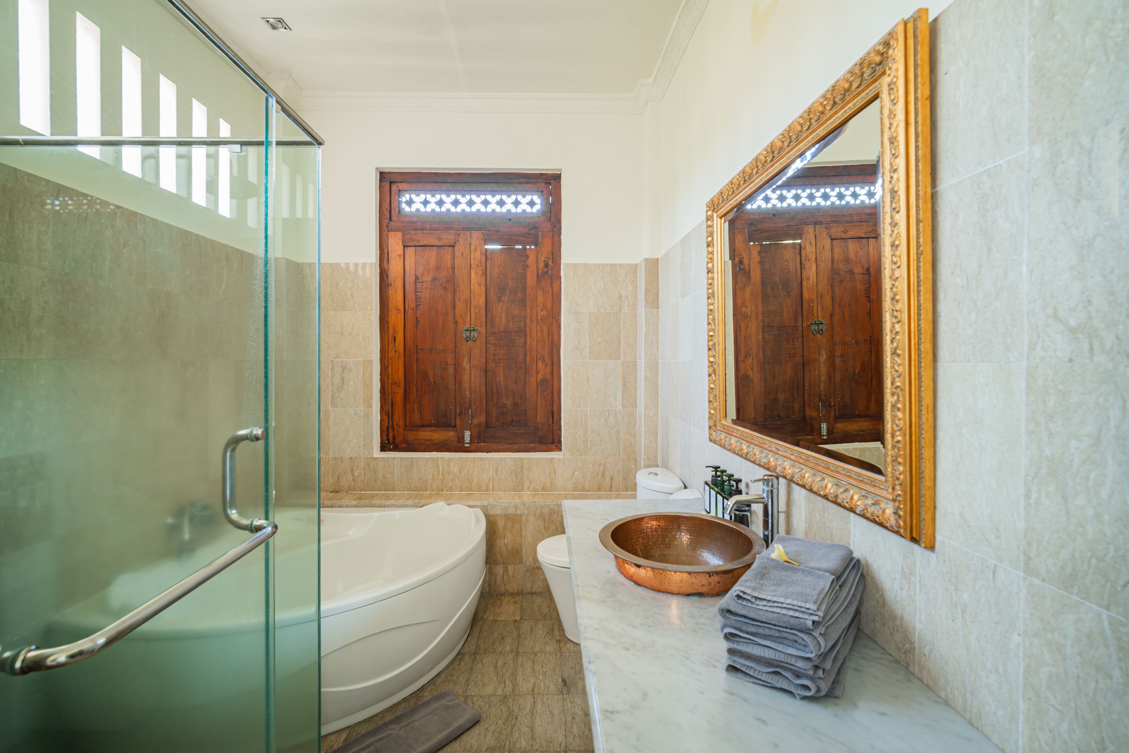A modern bathroom with a glass shower enclosure, a freestanding bathtub, a large mirror, and a copper basin.