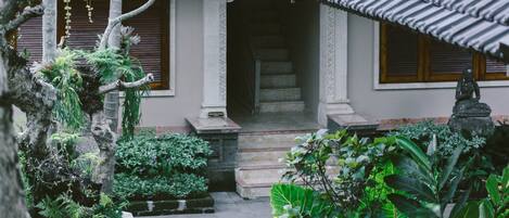 A traditional building with a tiled roof, a stone statue, and lush greenery.