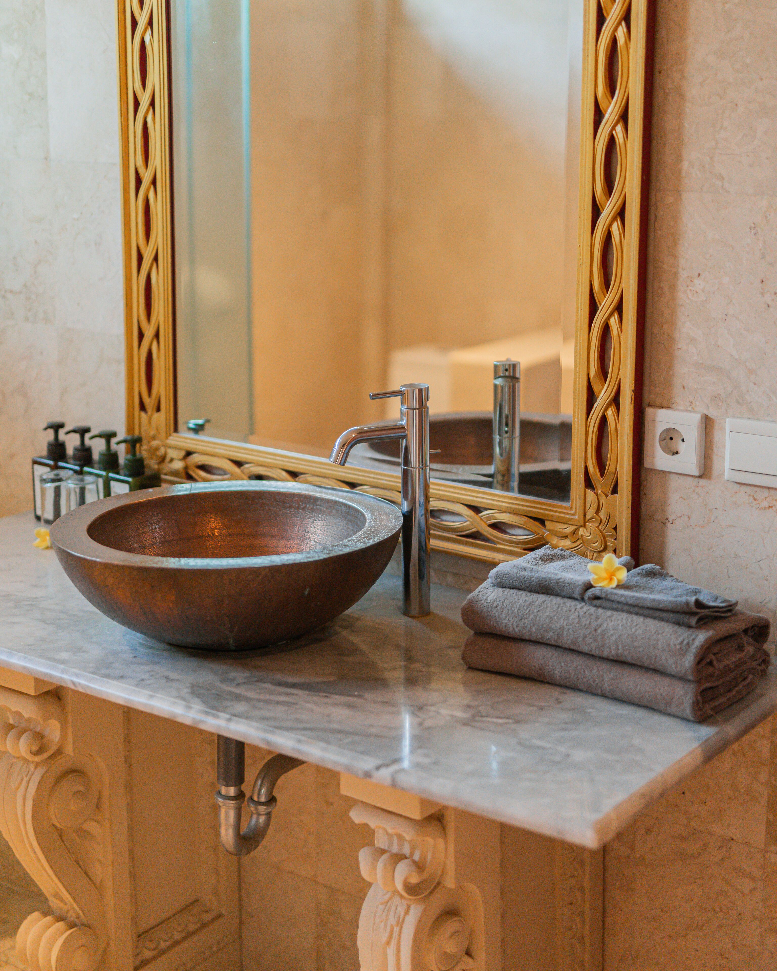 A bathroom vanity with a copper basin, a modern faucet, and a mirror with ornate framing.