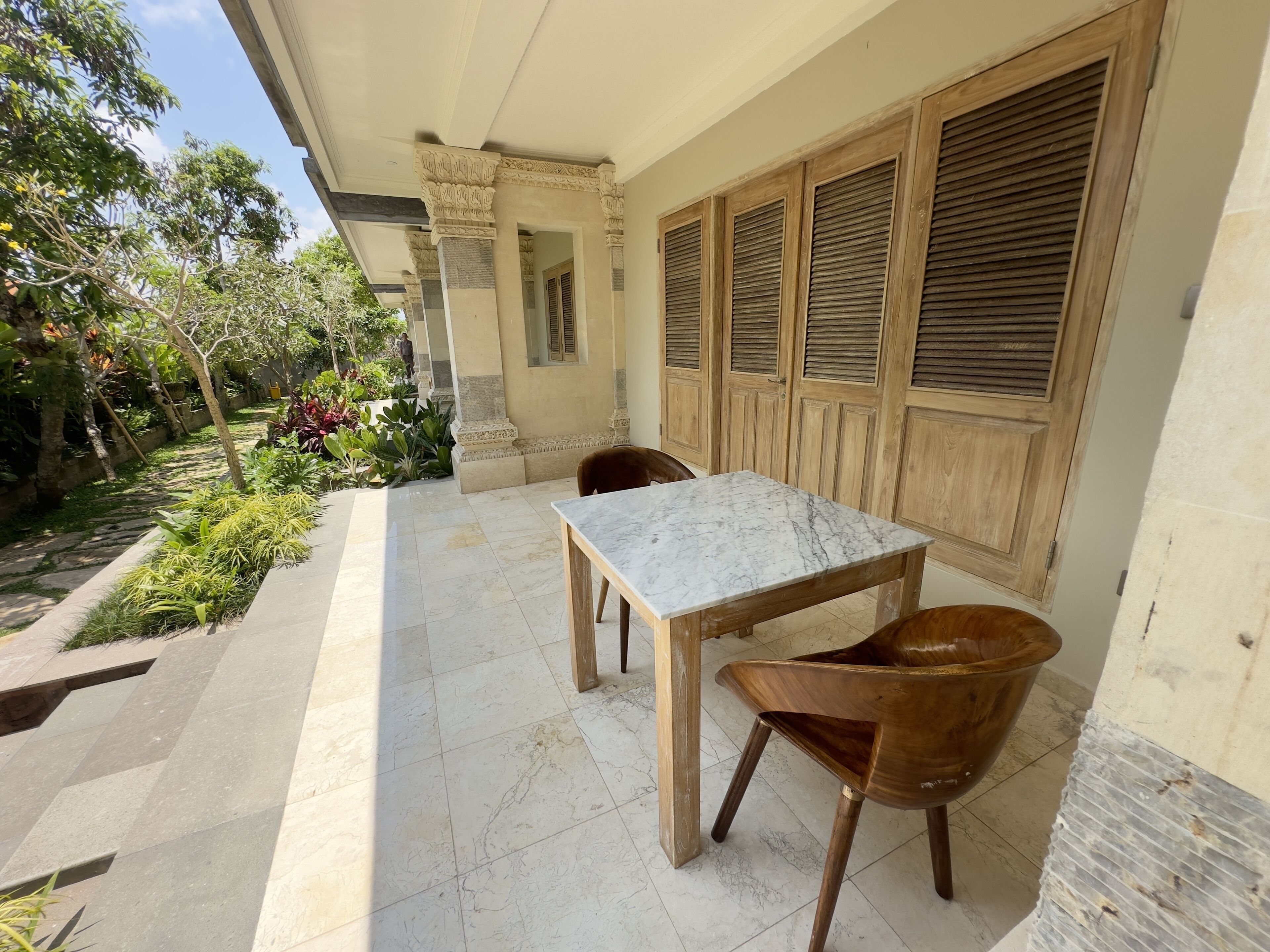 A patio with a marble table and wooden chairs, surrounded by plants and a garden.