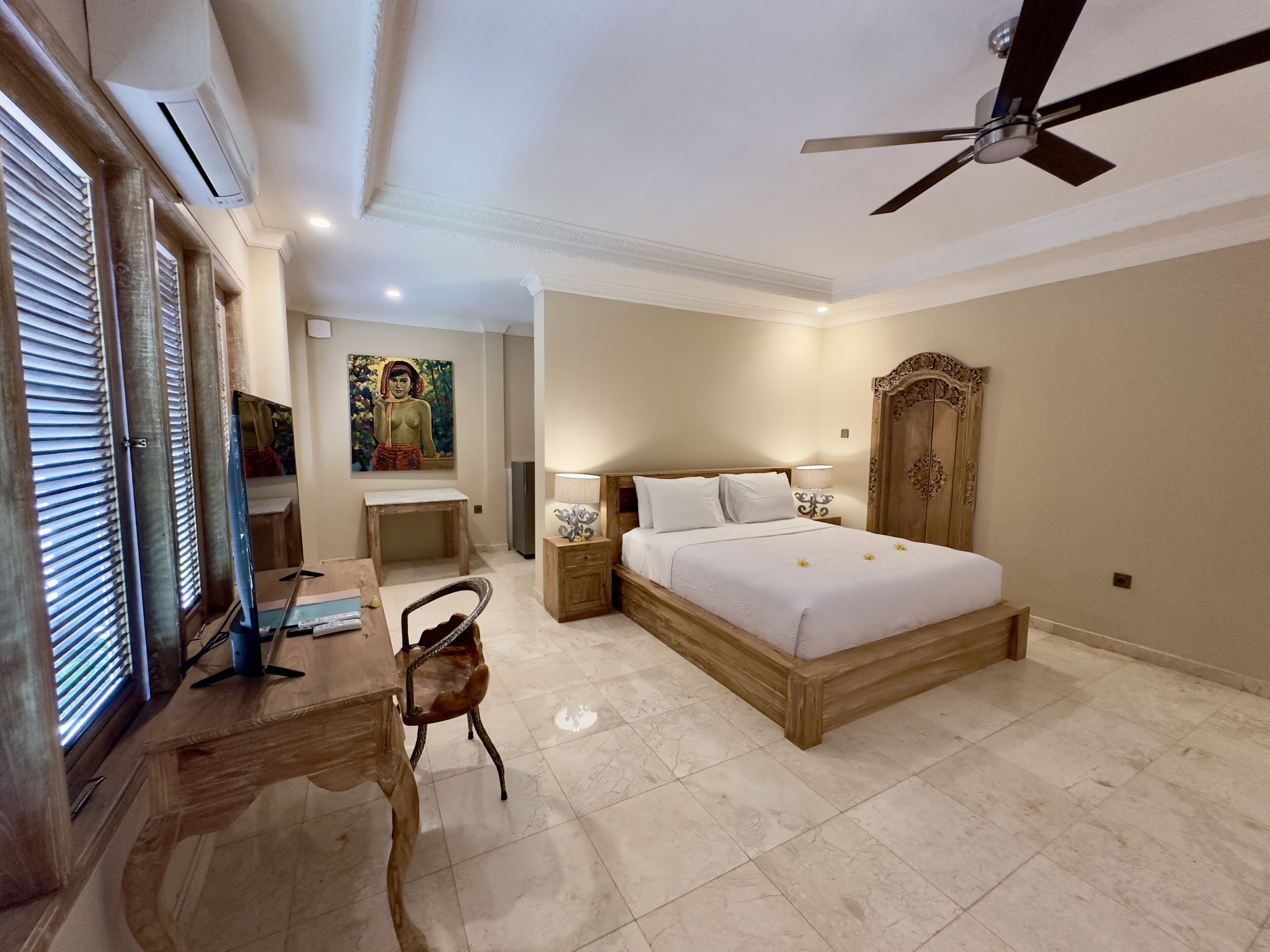 A bedroom with a bed, a desk, a chair, a ceiling fan, and a painting on the wall.