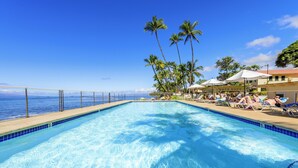 Ein Pool mit Blick auf den Ozean, umgeben von Palmen und Liegestühlen.