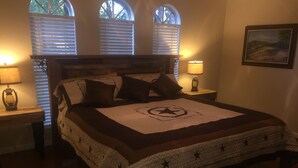 A neatly made bed with a star-patterned bedspread, two bedside lamps, and a window with blinds.