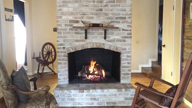 A living room with a stone fireplace, a rocking chair, and a vintage wagon wheel.