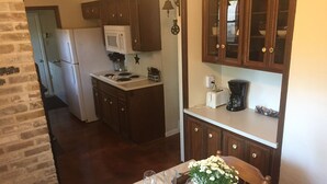 A kitchen with wooden cabinets, a microwave, and a coffee maker. There is a dining table with a vase of flowers and a plate with cutlery.