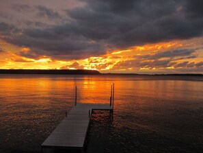 En träbrygga som sträcker sig ut i stilla vatten, med en solnedgång i bakgrunden.