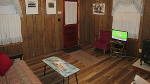 Una sala de estar con paredes de madera, un sillón rojo, un televisor y una mesita con una revista.