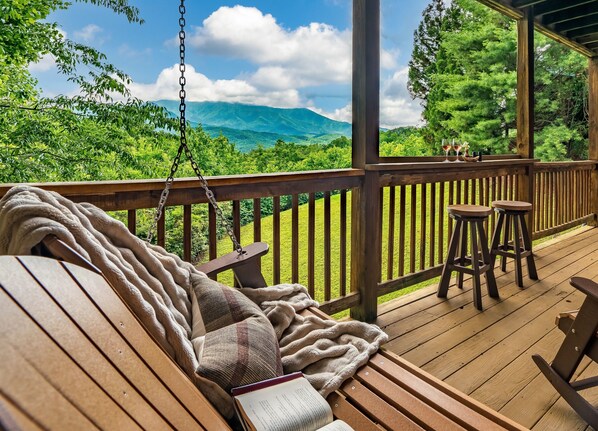 A wooden deck with a swing chair, a cushioned bench, and two stools.