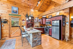 A wooden cabin interior with a stone island, bar stools, a kitchen with red cabinets, and a large refrigerator.