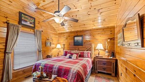Ein gemütliches Schlafzimmer in einer Blockhütte mit einem Bett, zwei Nachttischen, einem Deckenventilator und einem Fenster mit Vorhängen.