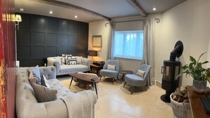 A modern living room with a sofa, armchairs, a coffee table, a fireplace, and a large window. - Beautiful 3 bed cottage in Lymington. Perfectly located for Coast and New Forest (Lymington)