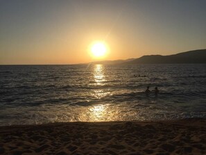 A beach with the sun setting over the water, people in the water, and a distant mountain range. - Awesome residence with a pool and a great view (Propriano)