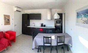 A compact kitchen with modern appliances, a dining area with a table and chairs, and a red chair in the living space.