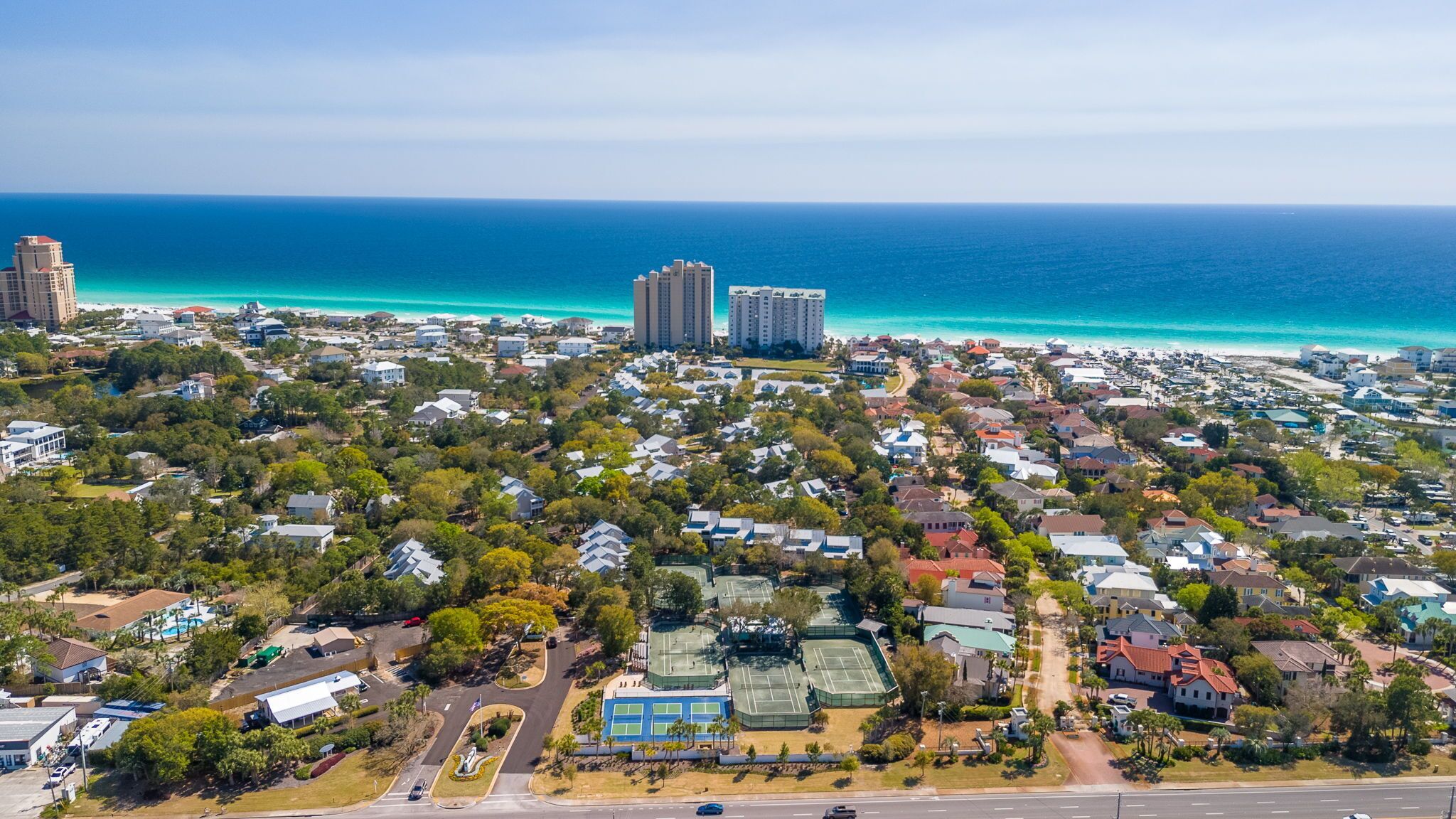 An aerial view of a coastal residential area with houses, a road, and a beach.