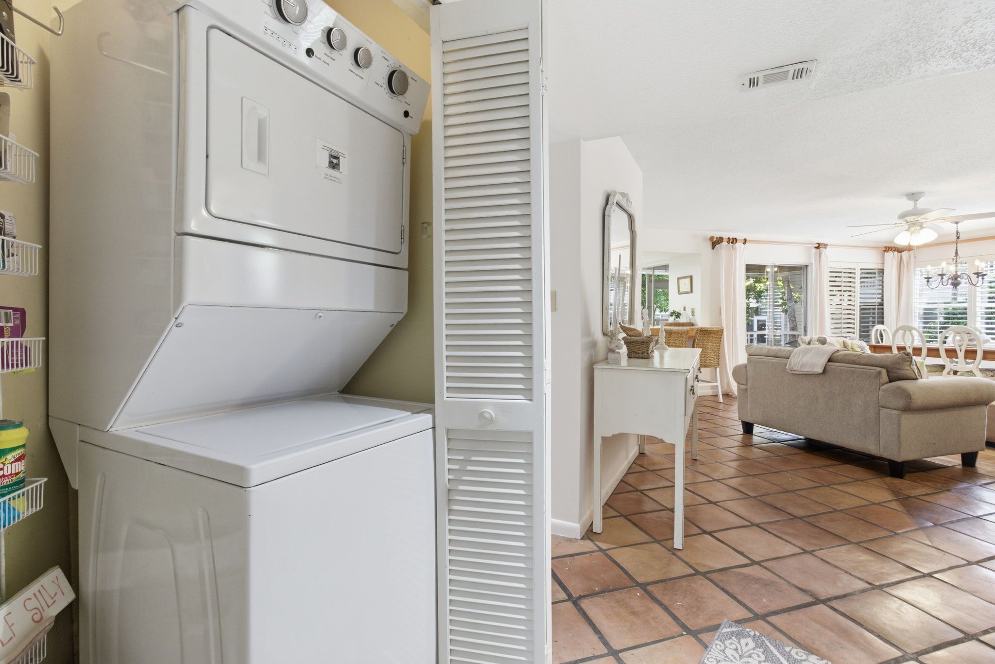 Un espace buanderie avec des machines à laver et des sèche-linge superposés, une commode blanche avec un miroir, un canapé beige et un sol carrelé.