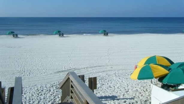 A beach with several umbrellas and a wooden walkway leading to the water.