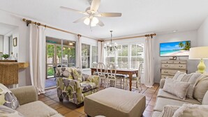 A living room with a ceiling fan, a dining table with chairs, a sofa set, and a TV on the wall.