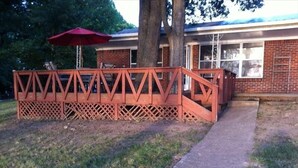 Eine Holzterrasse mit einem roten Sonnenschirm, ein Backsteinhaus und ein Weg zum Gebäude.