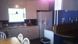 Eine kompakte Küche mit weißen Schränken, einem Kühlschrank, einer Spüle und einem Essbereich mit Tisch und Stühlen.