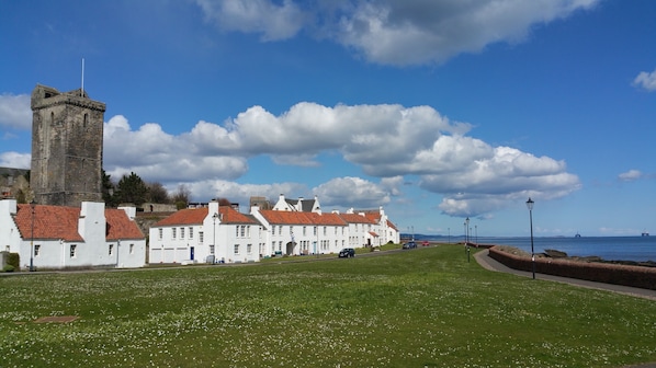 A coastal town with white buildings, a prominent tower, and a grassy promenade.