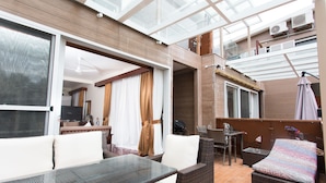 Un amplio patio interior con techo de vidrio, mobiliario de mimbre y televisor.