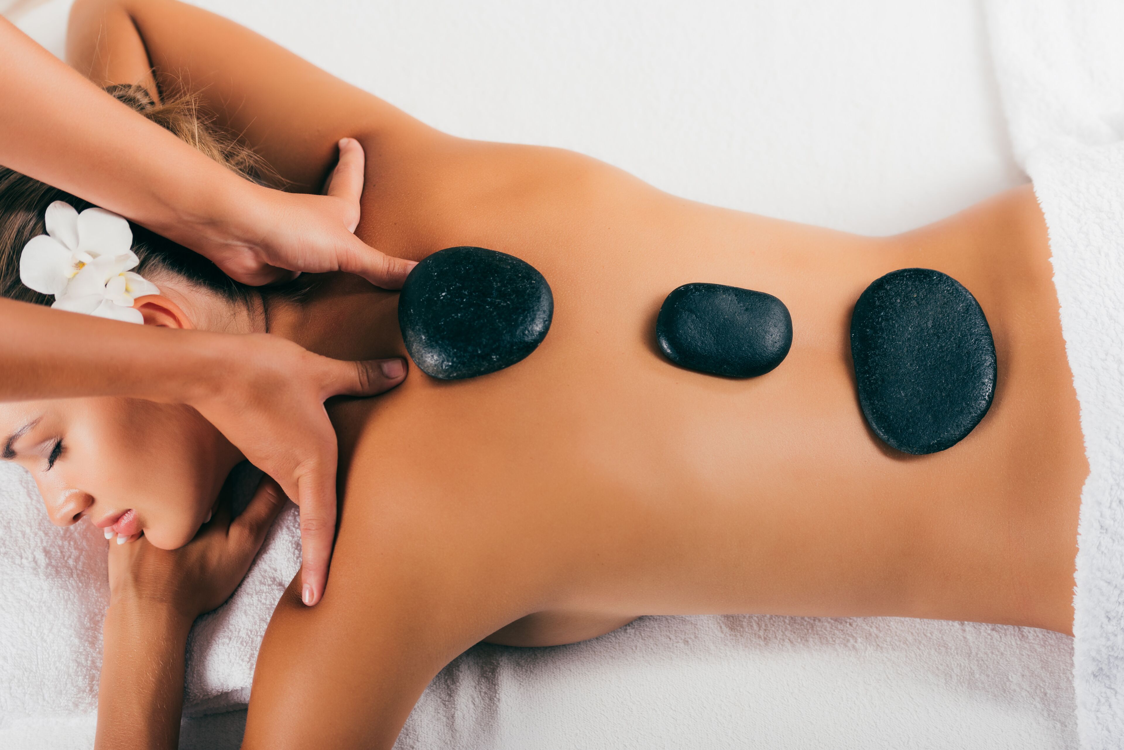 A person receiving a back massage with stones placed on their back.