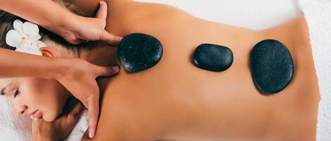 A person receiving a back massage with stones placed on their back.