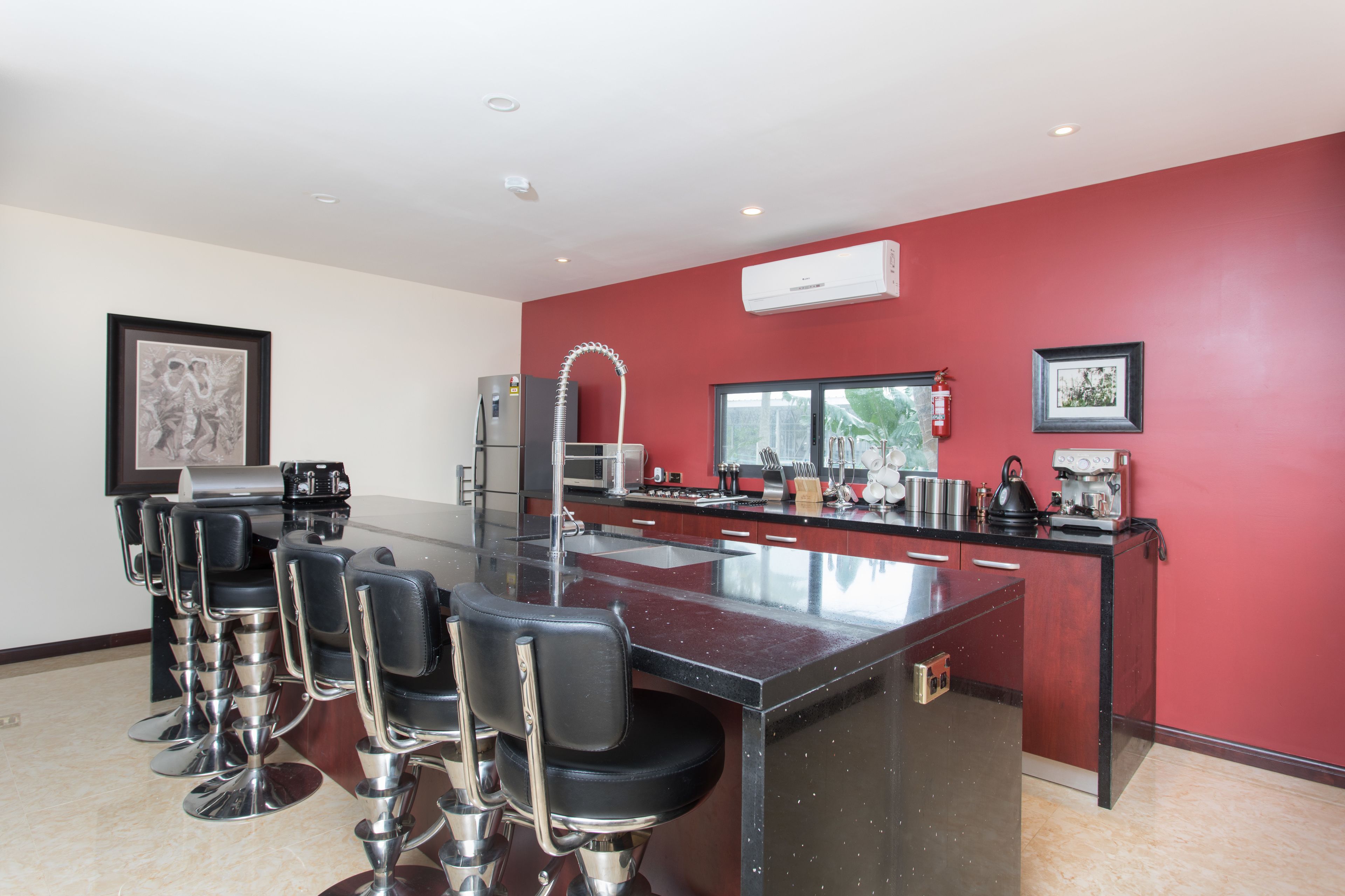 A modern kitchen with a central island, bar stools, stainless steel appliances, and red walls.