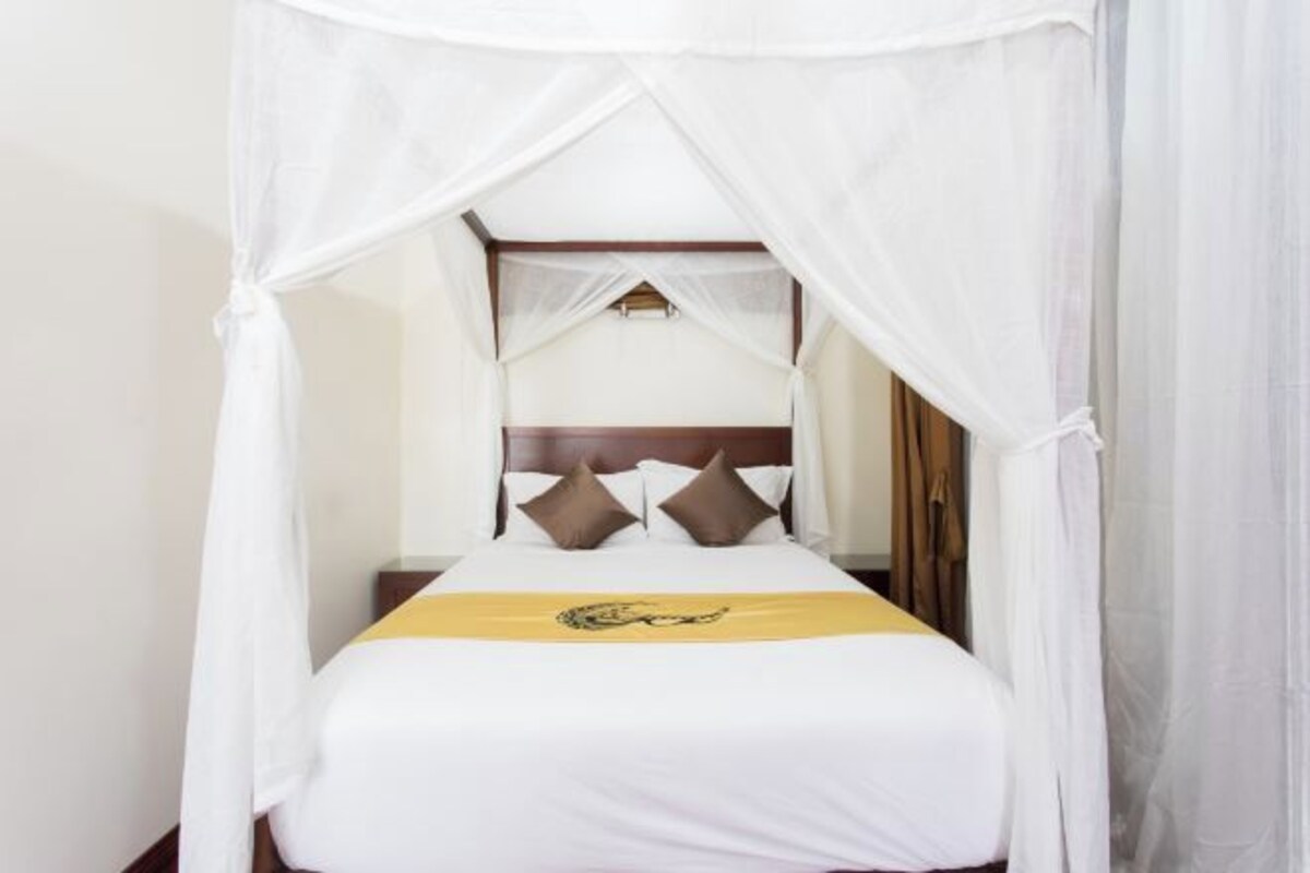 Una cama con dosel, ropa de cama blanca y una colcha amarilla.
