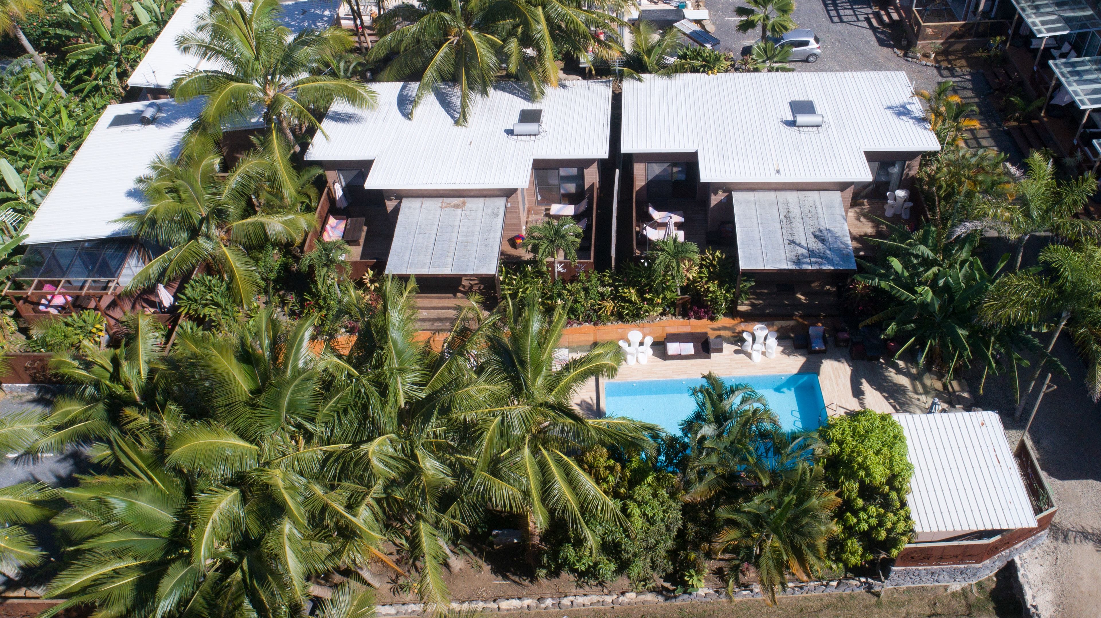 An aerial view of a resort with multiple buildings, a swimming pool, and lush palm trees.