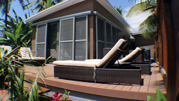 Un edificio moderno con un área exterior cubierta que incluye dos sillones y una mesita.