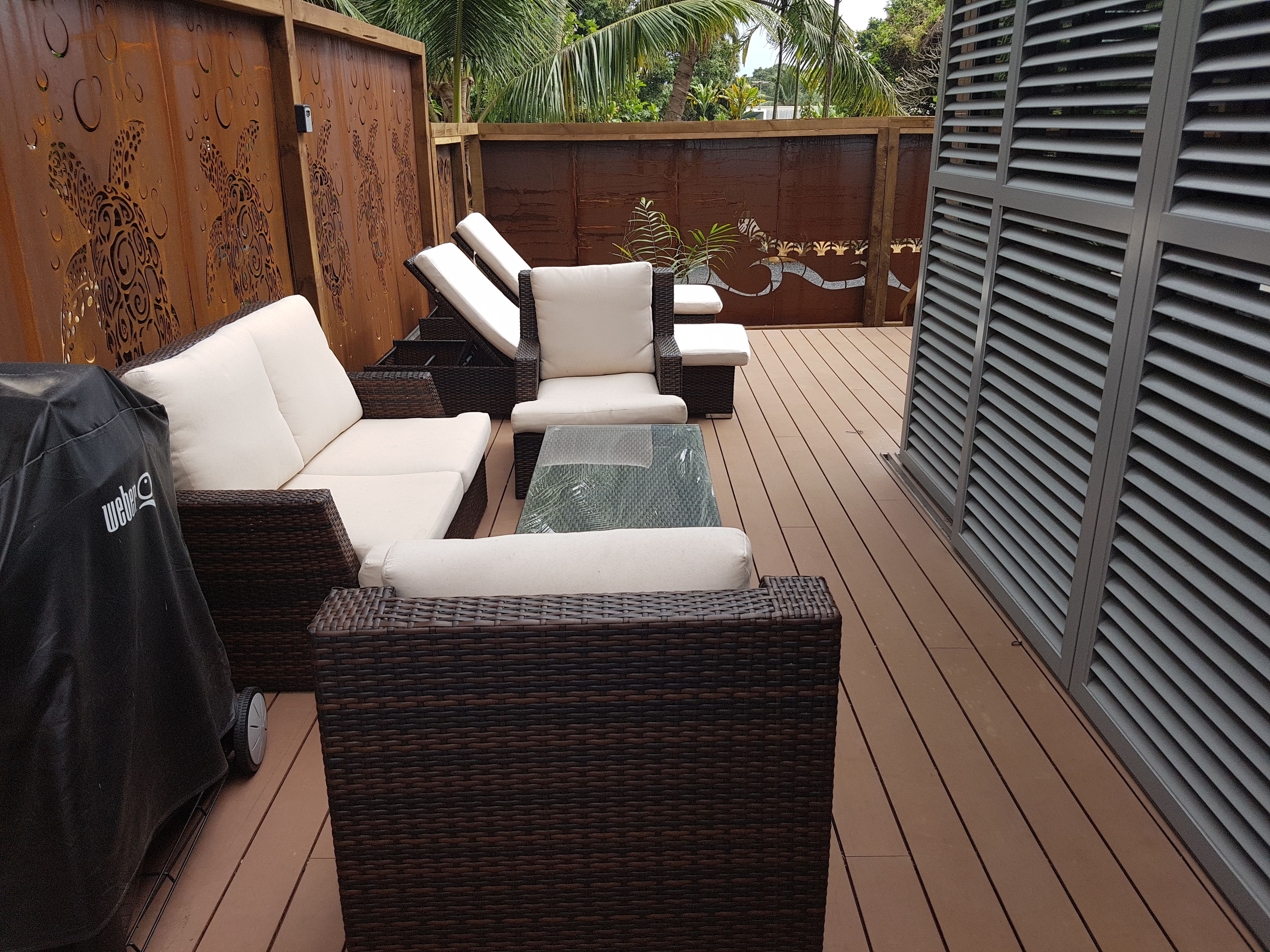 A patio with wicker furniture, a glass table, and a grill.