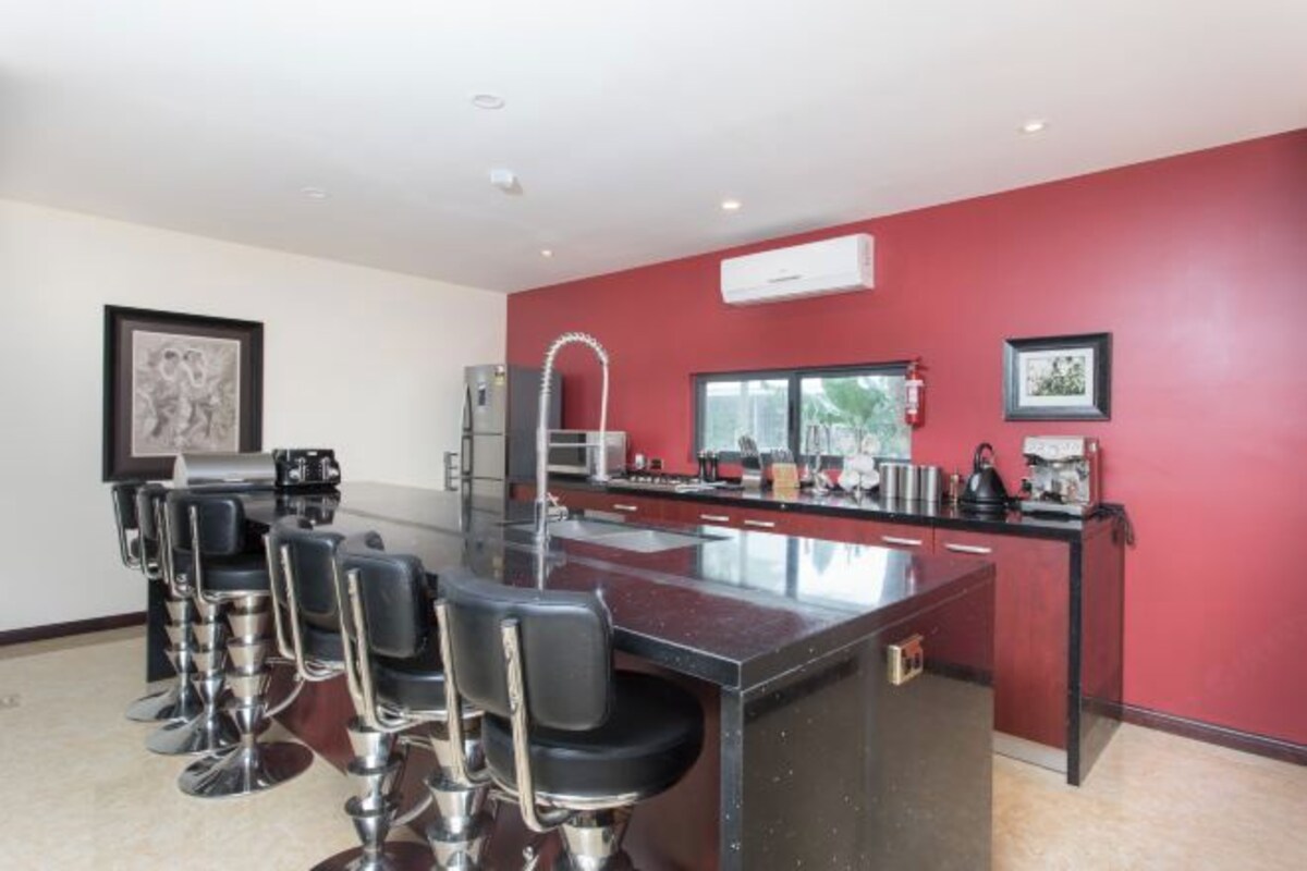 Una cocina moderna con una pared de acento roja, una isla central con taburetes y un ventanal que proporciona luz natural.