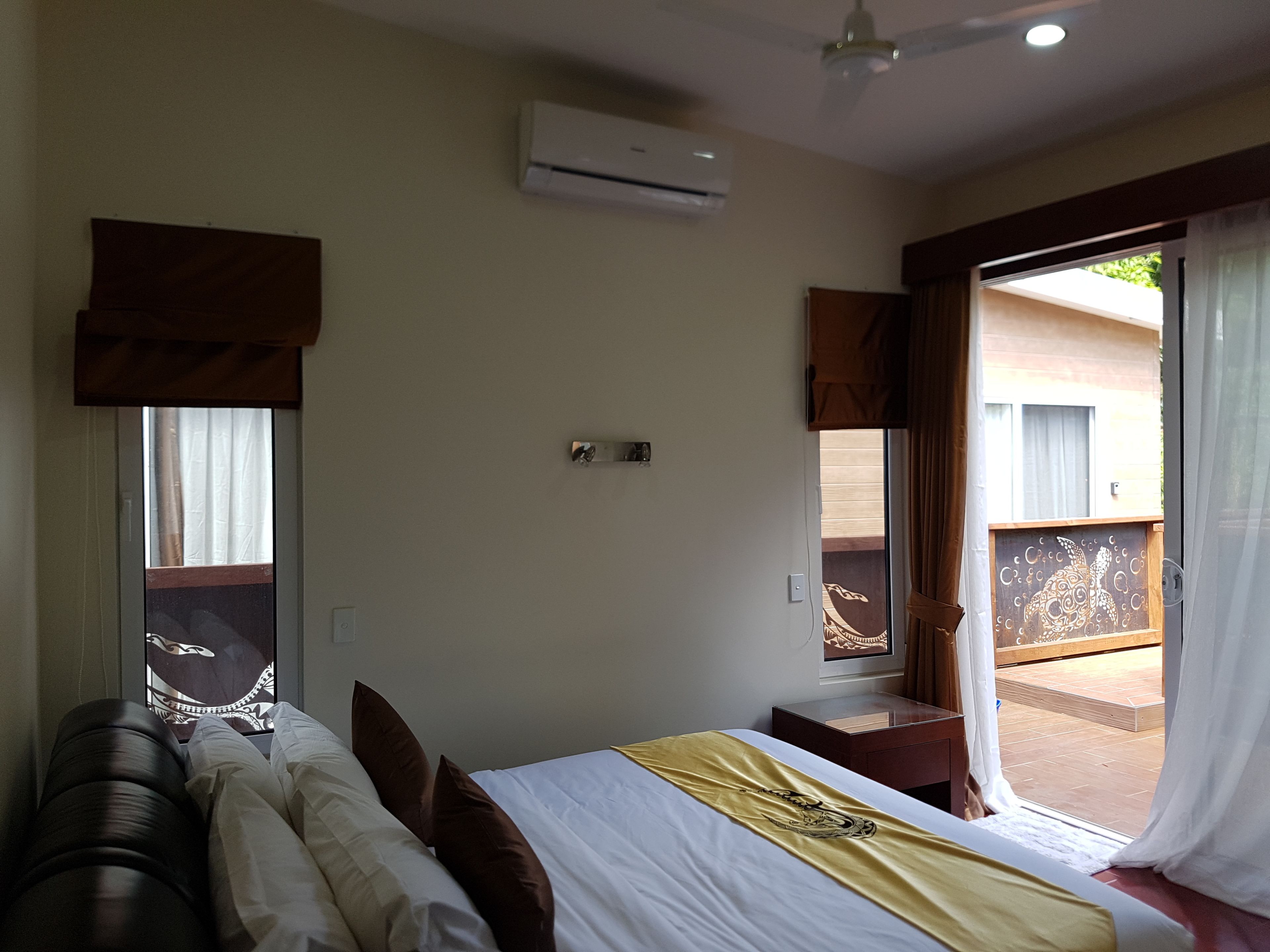 Ein Hotelzimmer mit Bett, einem Fenster mit Vorhängen, einer Klimaanlage und Blick auf den Balkon.