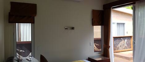 Ein Hotelzimmer mit Bett, einem Fenster mit Vorhängen, einer Klimaanlage und Blick auf den Balkon.