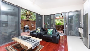 Una sala de estar moderna con un sofá de cuero negro, una mesa de centro de madera y un ventanal de vidrio que da a un patio con plantas.
