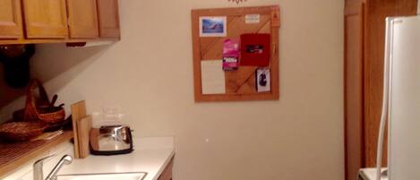 A small kitchen with wooden cabinets, a white sink, a stove, and a corkboard on the wall.