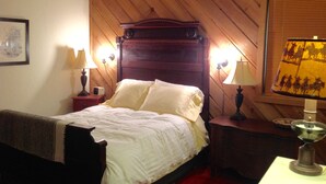 Ein Zimmer mit Holzwänden, einem Bett, zwei Nachttischlampen, einem Nachttisch und einer Wandlampe.