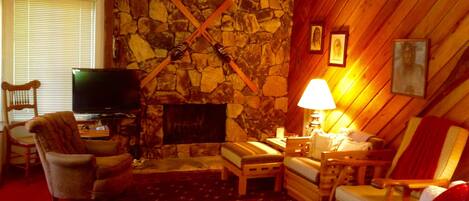 Un salón acogedor con chimenea de piedra, paredes de madera, televisor y asientos cómodos.
