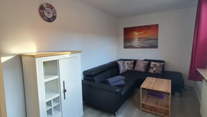 Ein Wohnzimmer mit einer schwarzen Couch, einer weißen Kommode, einem Holztisch und einer Wanduhr.