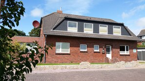 Ein zweistöckiges Haus mit Ziegelverblendung, zahlreichen Fenstern und einer Satellitenschüssel.
