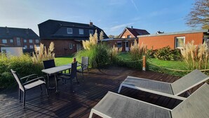Eine Holzterrasse mit Gartenmöbeln, eine Rasenfläche und ein Backsteinhaus im Hintergrund.