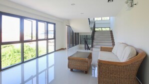 A spacious living area with large windows, a staircase, wicker furniture, and a clean, modern design. - HuaHin City View (Hua Hin)
