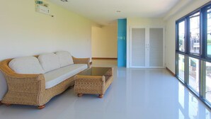 A spacious room with a wicker sofa and a matching ottoman, a large window with a view, and a door leading to another room. - HuaHin City View (Hua Hin)