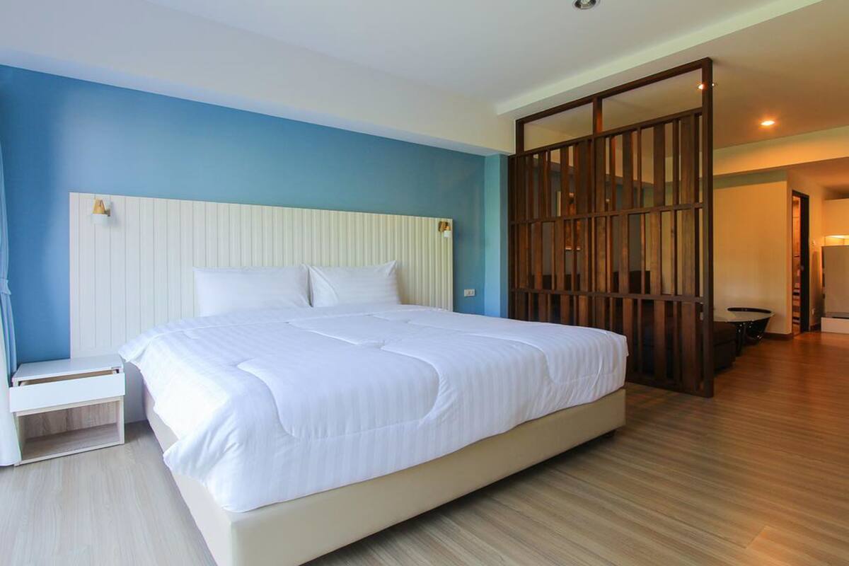 Un dormitorio con una cama grande, una mesita de noche, un separador de madera y vistas al baño.