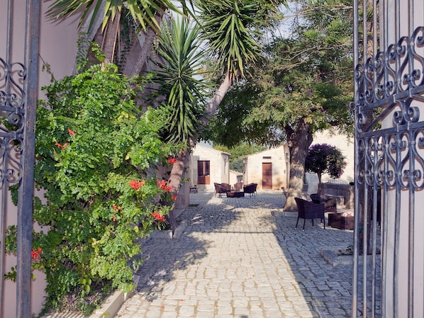 A cobblestone pathway leading to a courtyard with outdoor seating and a stone building.