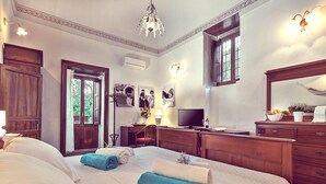 A hotel room with a large bed, wooden furniture, a television, and a window with a view of greenery. - Resort Borgo La Fasana formula (RG)
