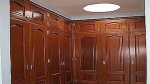 Ein Zimmer mit großem Holzschrank, Teppichboden und einer eingelassenen Deckenleuchte.