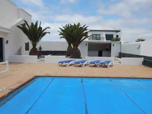 A pool area with blue lounge chairs, palm trees, and a white building with a balcony.